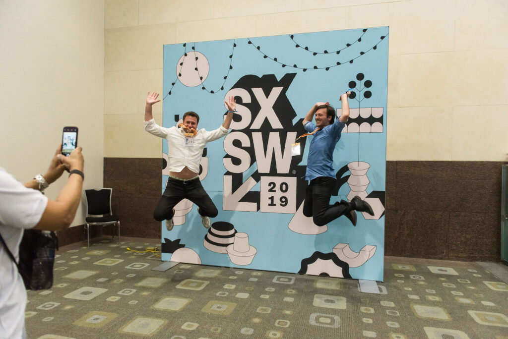 Attendees jump for joy at SXSW in front of a banner