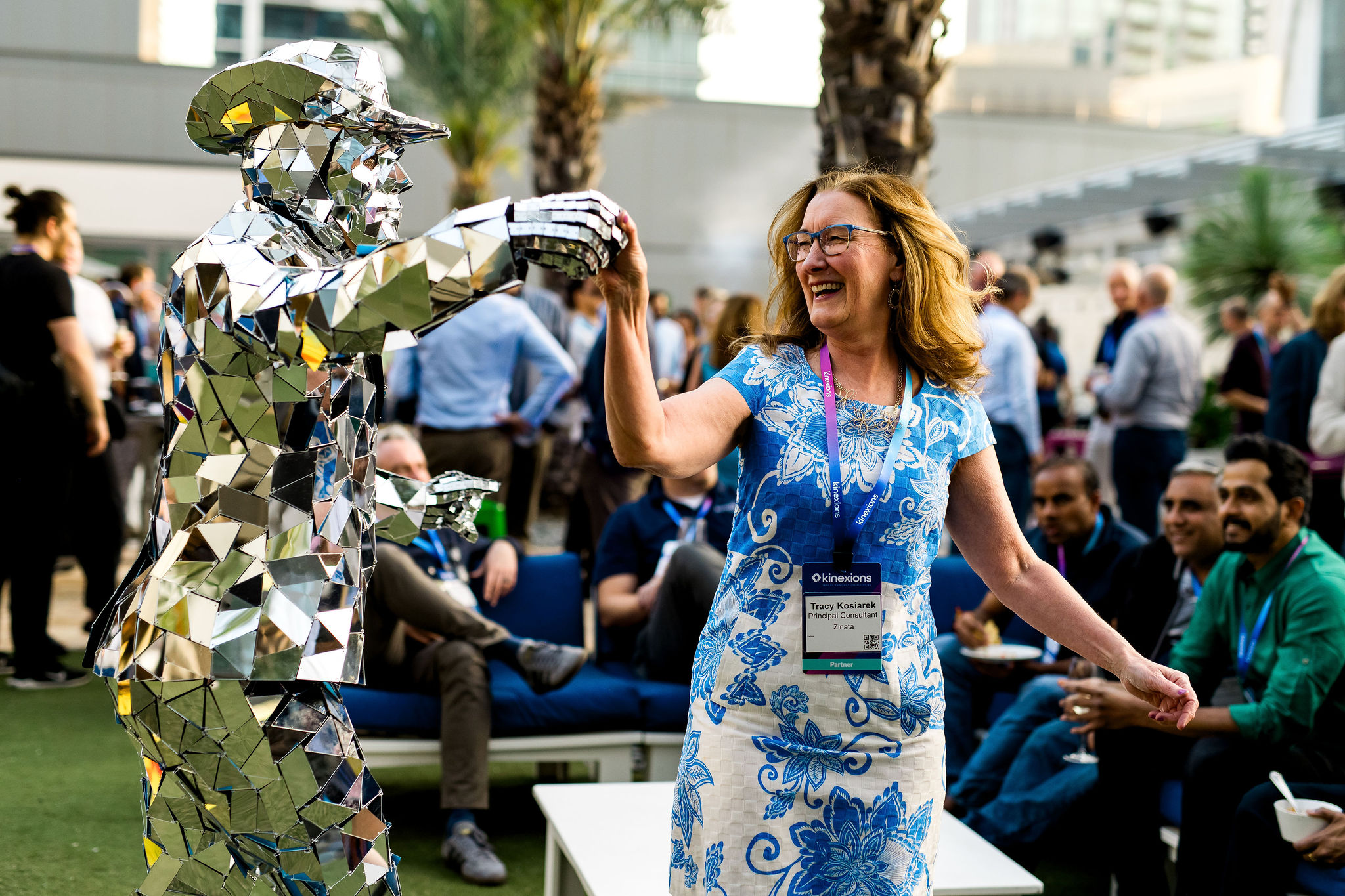 Kinexions A woman dances and laughs with a mirrored cowboy performer during an outdoor reception at Kinexions, as other attendees watch and mingle.