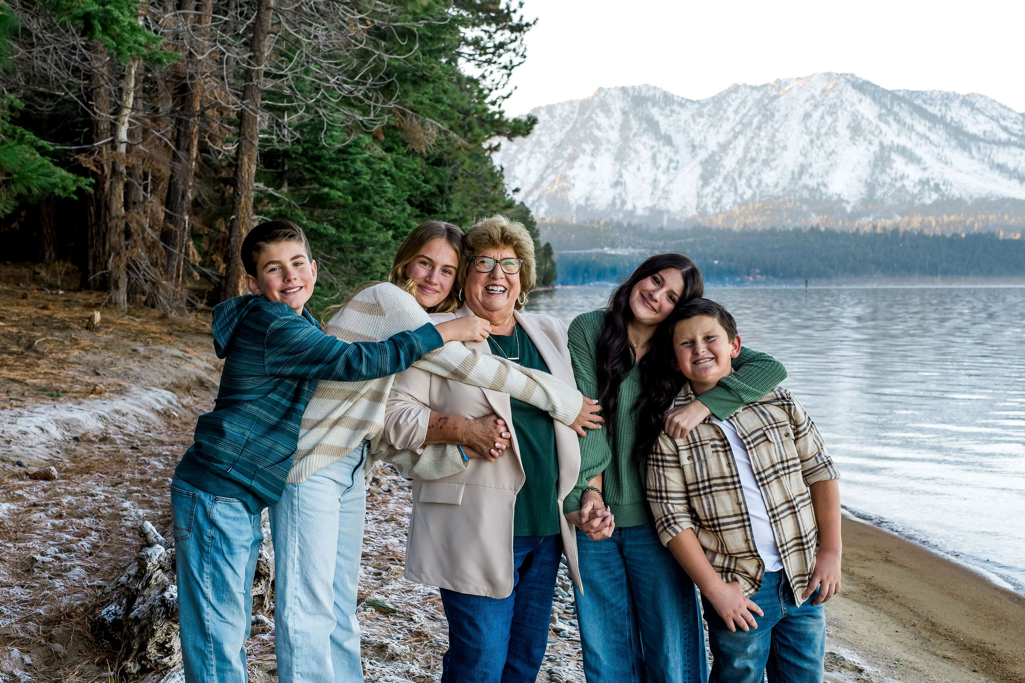 A grandmother and her 4 grandchildren embrace on the beach in a portrait at Valhalla Estate in South Lake Tahoe, Ca